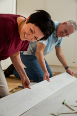 Senior couple installing laminate flooring in their new home together. DIY concept. Mature woman and man are doing renovation.