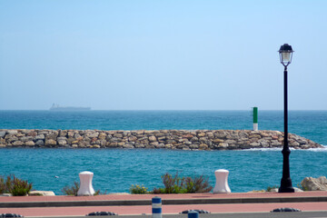 Calm image of the coast of Tarragona, showing a lighthouse, a rocky breakwater and the blue sea...