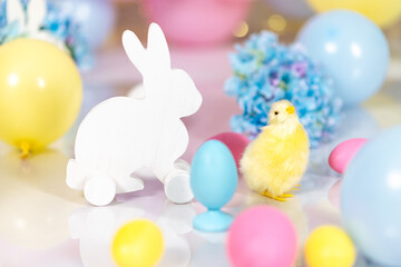 A figurine of a white Easter bunny against a background of Easter eggs, multi-colored pastel balls and blue hydrangeas