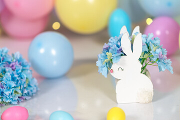 A figurine of a white Easter bunny against a background of Easter eggs, multi-colored pastel balls and blue hydrangeas