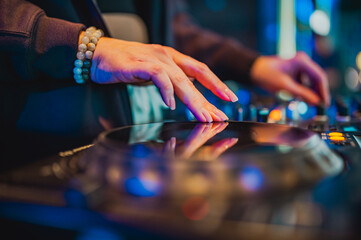 DJ’s hands skillfully manipulate a mixer, creating vibrant music, highlighted by the ambient...