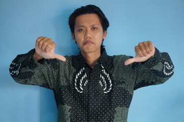 Portrait Asian man wearing a batik shirt, posing with a thumbs-down gesture, as if expressing disapproval