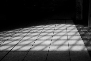 Square tile floor has a crosshatch shadow across the black background.
