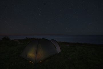 Camping with a tent in nature by the sea at night under the starry sky in Estonia.