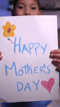Cheerful caucasian kid holding a Mother's Day banner and looking at camera happily. Vertical footage.