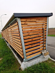 pergola roof with bus stop. combined with bin sorting. plastic, paper, glass separated into colored bins. wooden slats, blue sky, clouds, broom, trowel, sidewalk, street