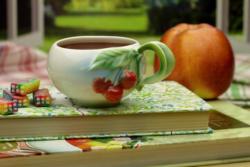 A beautiful cup of tea, sweets and an apple on the windowsill. Summer still life in the form of tea and fruit close-up. You can see the landscape outside the window.