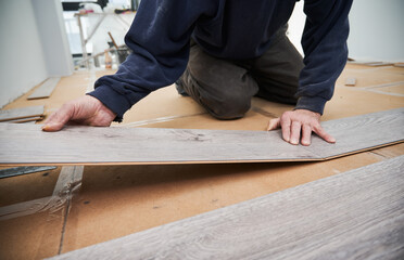 Close up of man hands laying laminate wooden planks on the floor in apartment under renovation. Male construction worker installing timber laminate flooring at home. Hardwood floor renovation concept.