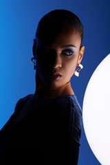 A young African American woman captivated by a white sphere in a studio setting.