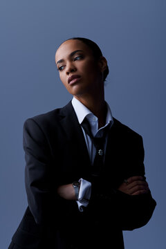 A young African American woman confidently poses in a suit and tie for a portrait in a studio setting.