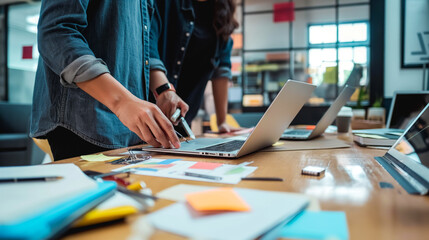 Two colleagues collaborating on a project with laptops and notepads at an open-space office table.