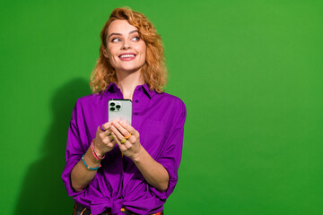 Photo portrait of pretty young girl hold gadget look empty space wear trendy purple outfit isolated on green color background