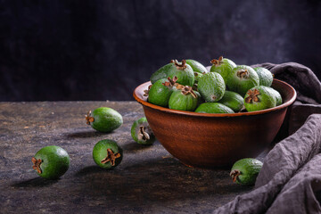 Tropical fruits green ripe feijoa sellowiana berries in a clay bowl and on a table on a dark background with copy space for text
