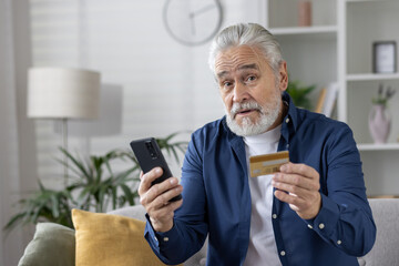 Senior man holding credit card and smartphone at home - obrazy, fototapety, plakaty