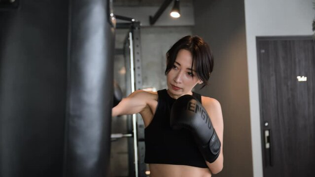 Frontal close-up video of a cool, handsome boxer woman punching and boxercising at the gym.