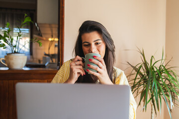 One young girl or woman is using her laptop to work from home in the morning while drinking coffee
