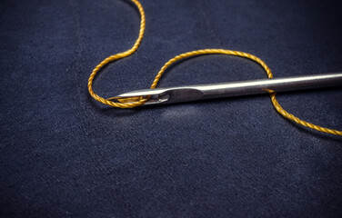 A needle with a thread is on a blue surface.