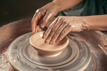 A person is making a bowl out of clay. The bowl is in the center of the image and the person is using their hands to shape it. The bowl is not yet finished