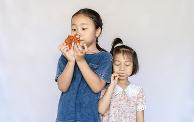 Close up portrait of two satisfied adorable Asian girls eating fried chicken. Happy small hungry kids biting fried chicken and enjoying a meal together. Children's healthy diet. Unhealthy food concept