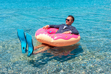 Happy businessman in flippers on an inflatable donut in the sea.
