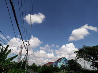 High voltage line wires and pole against beautiful blue cloudy sky passing small road and public...