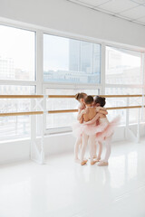 Cute little girls, ballerinas hugs in group while training near barre in light modern dance studio....