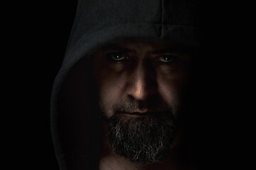 Close-up portrait of a man with a hood on a black background. Mysterious man wearing hoodies