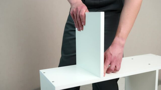Furniture assembly. Furniture assembler takes white shelf, installs it in right place. Moving concept, furniture assembler, self-assembly.