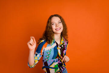 Photo of cheerful positive girl wear trendy print clothes have fun look empty space isolated on vibrant orange color background