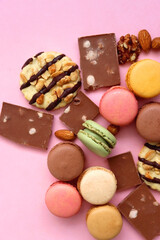 Pastel macarons, almond chocolate, peanut butter cookies and various nuts on bright pink background. Top view.