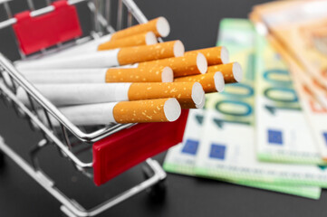 Shopping cart with cigarettes and euro bills on black.