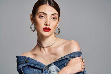 Brunette woman slaying in a denim dress, with striking red lips, exuding confidence and style in a studio setting. - obrazy, fototapety, plakaty