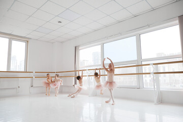 Children in tutus posing in different poses during ballet session near barre at modern dance...
