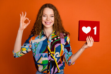 Photo of lovely girl wear stylish clothes hold red heart symbol okey sign isolated on vivid orange color background