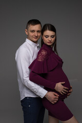 portrait of a pregnant couple, pregnant couple stands on a grey background in a studio, studio pregnancy photo shoot, pregnant woman posing in a studio, pregnant, pregnancy