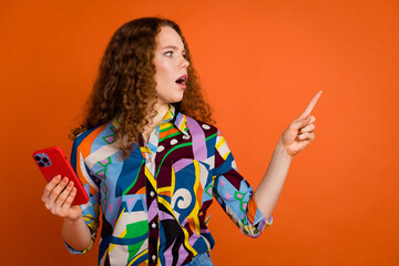 Photo of shocked confused woman wear trendy print clothes look empty space isolated on vibrant orange color background