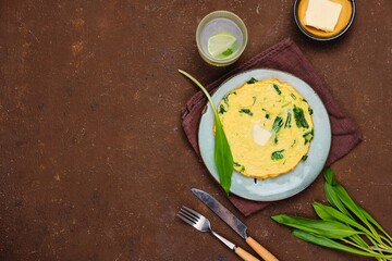 Breakfast, omelette with wild garlic on a ceramic plate on a brown concrete background. Recipes with wild greens.