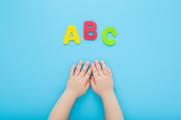 Baby boy hands and colorful abc letters on light blue table background. Pastel color. Time to learning. Closeup. Point of view shot. Top down view.