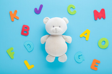 Smiling cute soft white teddy bear and colorful letters on light blue table background. Pastel color. Time to learning. Closeup. Top down view.
