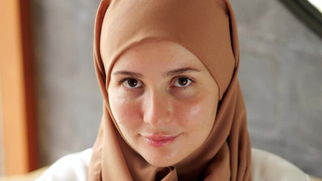 Young woman with covered hair move head slightly and looks at the camera with friendly and obedient look. Portrait shot with blurred background, the camera is slightly above the woman