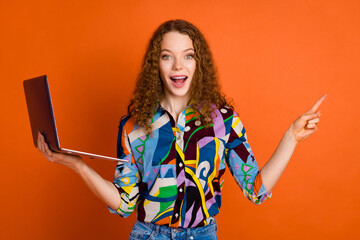 Photo of astonished glad girl wear stylish print clothes recommend buy device empty space isolated on orange color background