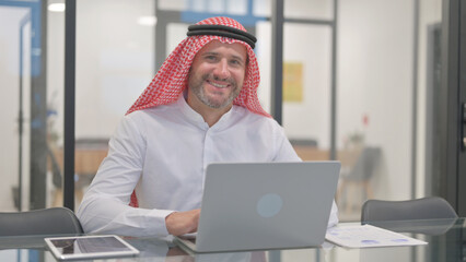 Arab Man Smiling at Camera while Working on Laptop in Office