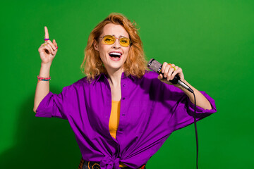 Photo portrait of pretty young girl singing hold microphone wear trendy purple outfit isolated on green color background