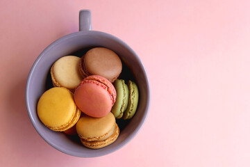 Purple cup filled with pastel macarons on pink background. Top view.