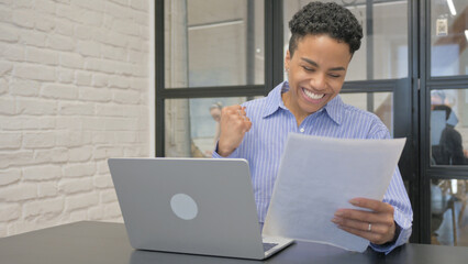 Young African Woman Celebrating while Working Laptop and Documents