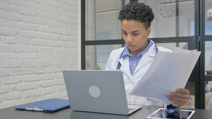African Female Doctor Working on Medical Documents and Laptop - obrazy, fototapety, plakaty