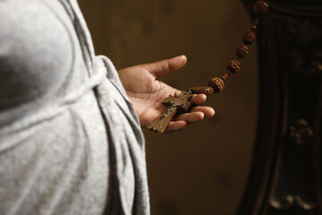Woman holding cross and prayer beads in a church in Eure, France