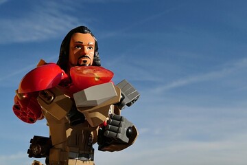 Fototapeta premium LEGO Star Wars Rogue One figure of Baze Malbus, holding small half sliced red cherry tomato on his right arm,blue skies with some wind blown clouds in background. 