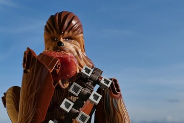 Obraz premium LEGO Star Wars large action figure of Wookie Chewbacca, also called Chewie, eating slice of red salami, blue skies in background. 