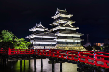 Japanese Castle and red bridge at night with a reflection in its moat
